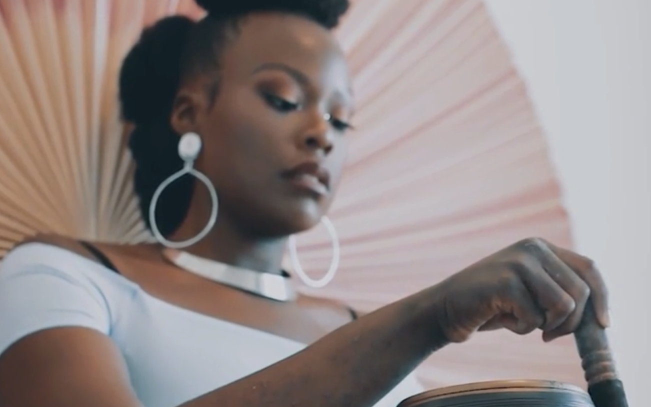 A black woman using a singing bowl and looking into it with deep concentration.